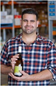 Profile photo of Lawrence Monforte standing in front of a rack holding a bottle of wine.